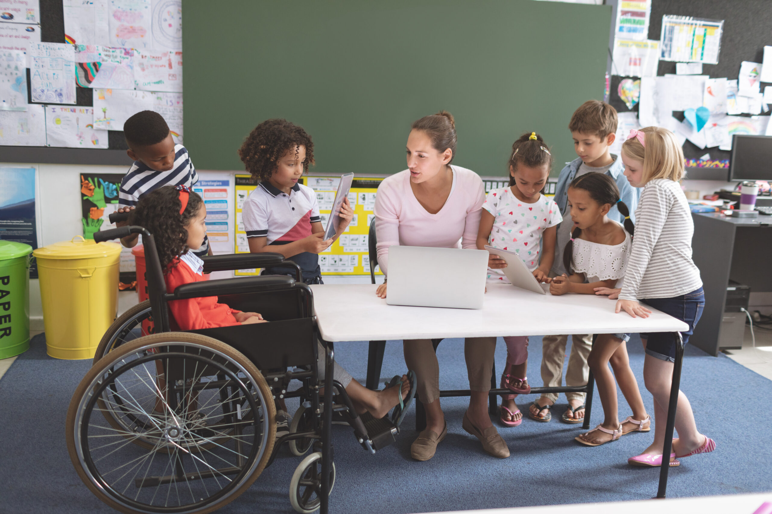 Students using digital tablet while teacher interacting with students in classroom at school